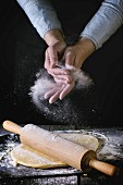 Female hands powdered by flour rolled out dough for pasta with wooden rolling pin