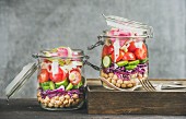 Vegetable and chickpea sprout vegan salad in glass jars, grey concrete wall background