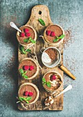 Tiramisu in glasses with mint leaves, fresh ripe raspberries and cocoa powder on rustic wooden board
