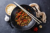 Stir fry beef meat with vegetables and rice in wok pan on dark stone background