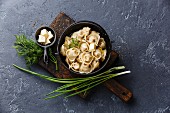 Russian pelmeni meat Dumplings with butter and greens in black iron pot on dark stone background