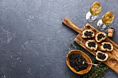 Sturgeon black caviar in wooden bowl, sandwiches and champagne on dark stone background