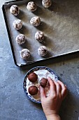 Making chocolate crinkle cookies.Female hand coating dough ball with icing sugar, top view