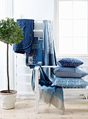 Kissen, Decken und Wohntextilien in Blautönen im Schlafzimmer, seitlich Zimmerbäumchen