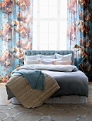 Pastel bed linen and blankets on double bed in front of curtains with pattern of angels