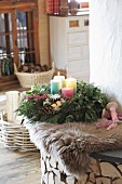 Advent wreath with four colourful candles on sheepskin rug on bench next to fireplace