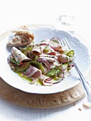 A sausage salad with pickled cucumbers and red onions