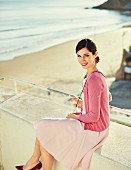 A brunette woman wearing a pink dress, pink cardigan and Bordeaux-red heels