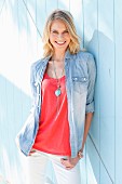 A blonde woman wearing a red top, a denim shirt, white trousers and a necklace