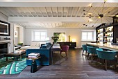 Blaues Polstersofa vor Kamin und langer Tisch mit Schalenstühlen in offenem Wohnraum mit weisser Holzbalkendecke