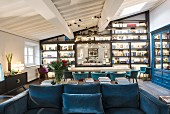 Blue sofa, long table, shell chairs and wall covered in shelves in open-plan interior