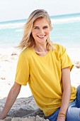 Blonde Frau in gelbem T-Shirt und Jeans am Strand