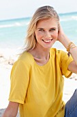 Blonde Frau in gelbem T-Shirt und Jeans am Strand
