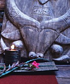 Lit candle in bowl and flower in front of ethnic carving