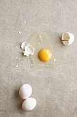 Two whole chicken eggs and one cracked one, on a grey background (seen from above)