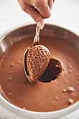 A quenelle of chocolate mousse being scooped out of a bowl with a spoon