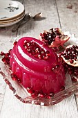 Glittery pink jelly covered in pomegrante seeds on a vintage glass dish with a split pomegrante in the background