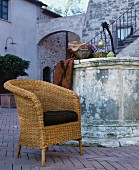 Wicker chair with seat cushion in front of vintage fountain in Mediterranean courtyard