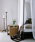 White candles in large black candlesticks next to bed with canopy and fur blanket