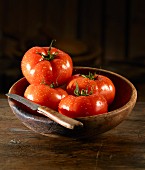 Tomatoes with drops of water and a knife in a wooden bowl