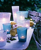 Teelichter in Glasgefässen zwischen Blüten und Zitronen als sommerliche Tischdeko
