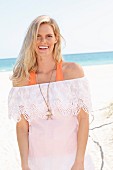 Blonde Frau in weißem schulterfreiem Top mit Spitzenborte am Strand