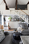 Grey sofa set, staircase and kitchen in open-plan interior