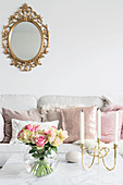 Spherical vase of roses and candelabra on coffee table and gilt-framed mirror above sofa with scatter cushions in background