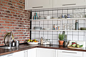 Open shelving, wooden worksurface and brick wall in white kitchen