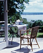 Korbstuhl und runder Tisch auf der Terrasse mit Blick auf den See