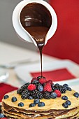 A pancake cake with berries and chocolate sauce