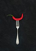 Red hot chili pepper on vintage silver fork over black slate stone background, top view