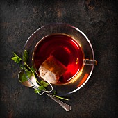 Eine Tasse Tee mit Teebeutel und Minze auf Metalluntergrund (Aufsicht)
