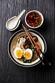 Ramen noodles with egg, enoki and shiitake mushrooms with broth on dark wooden background