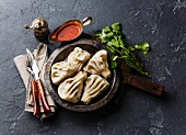 Georgian dumplings Khinkali with meat and tomato spicy sauce satsebeli on dark stone background