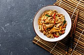 Udon stir-fry noodles with chicken in bowl on dark stone background copy space
