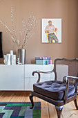 Old armchair with velvet seat cushion in front of white modern sideboard