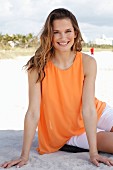 Blonde Frau in orangefarbenem Top und weißer Hose am Strand