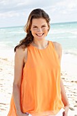 A young woman wearing an orange top and white trousers on the beach