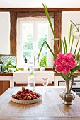 Strawberries, carafe of water and pewter vase of peonies on kitchen table