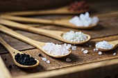 Different types of food coarse Salt in wooden spoons on dark background