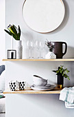Shelf with dishes and flower vase under a round wall mirror