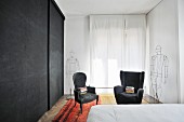 Schlafzimmer mit schwarzer Schrankwand und zwei Armlehnsesseln neben Draht-Skulpturen