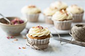Rose and lemon cupcakes with rosewater and lemon frosting tied with string with spoon and bowl of rose petals on a white and grey marble surface