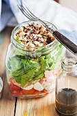 A mixed salad with plum tomatoes, mozzarella balls, salmon, lettuce and toasted hazelnuts, with a balsamic and hazelnut oil dressing in a glass jar
