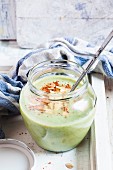 Spinach cream soup in a glass jar with roasted almonds and chilli flakes