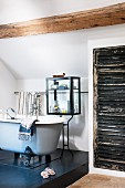 Free-standing, vintage-style bathtub on black platform in front of bath utensils in glass case