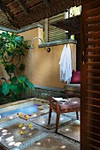 Flowers scattered in water and on stone-flagged floor in roofed showering area with wall-mounted shower head and bath