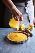 Female hand pouring lemon curd in a pastry shell