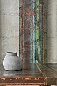 Vase aus Beton vor einem Kunstwerk aus Metall